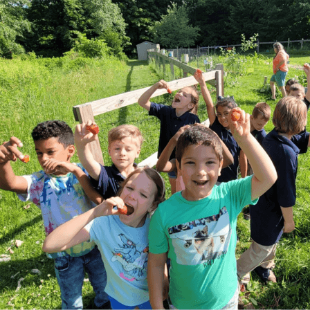 Many young students holding up fruits by the garden