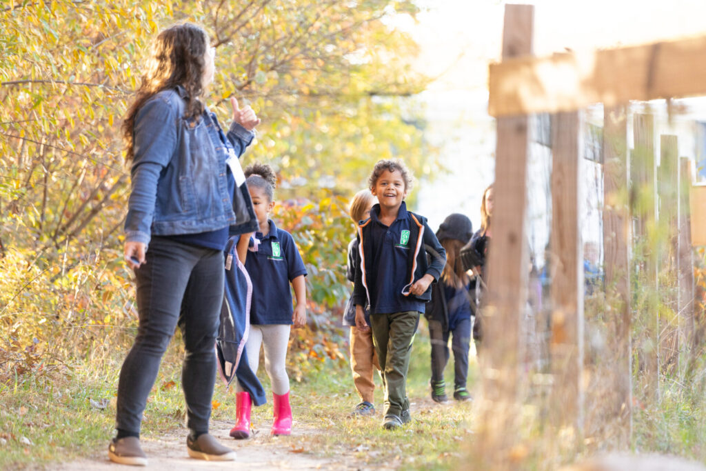 Children explore a sunny autumn path, guided by a caring adult, enjoying nature together.