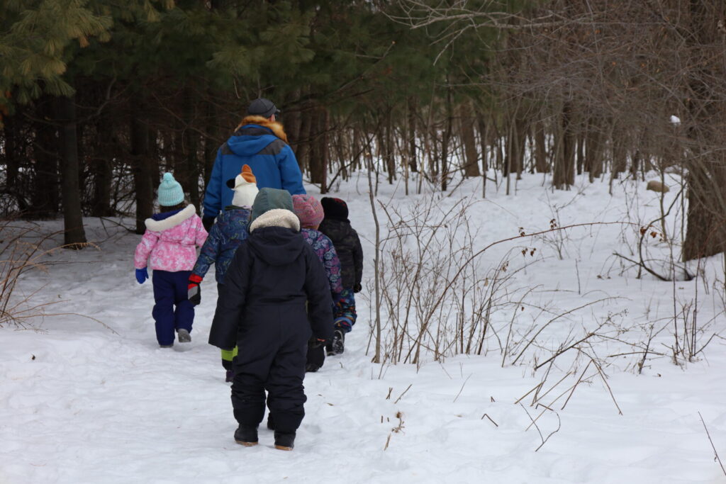 Children joyfully explore a snowy path in a winter forest with an adult guide.
